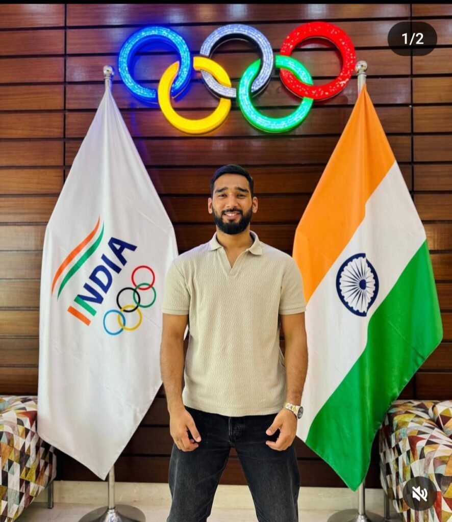 Anshul Jubli, an Indian MMA fighter, stands smiling between the Indian national flag and the Indian Olympic Association flag. The Olympic rings are illuminated in the background, symbolizing a connection to Indian sports and possibly the future of MMA in India on a global stage.
